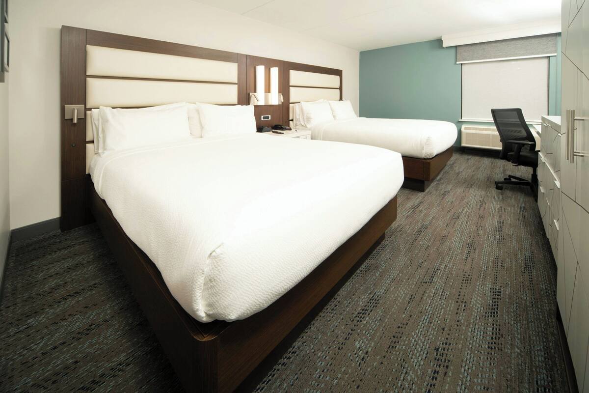 A hotel room with a large bed, a smaller bed, a desk, and a chair.