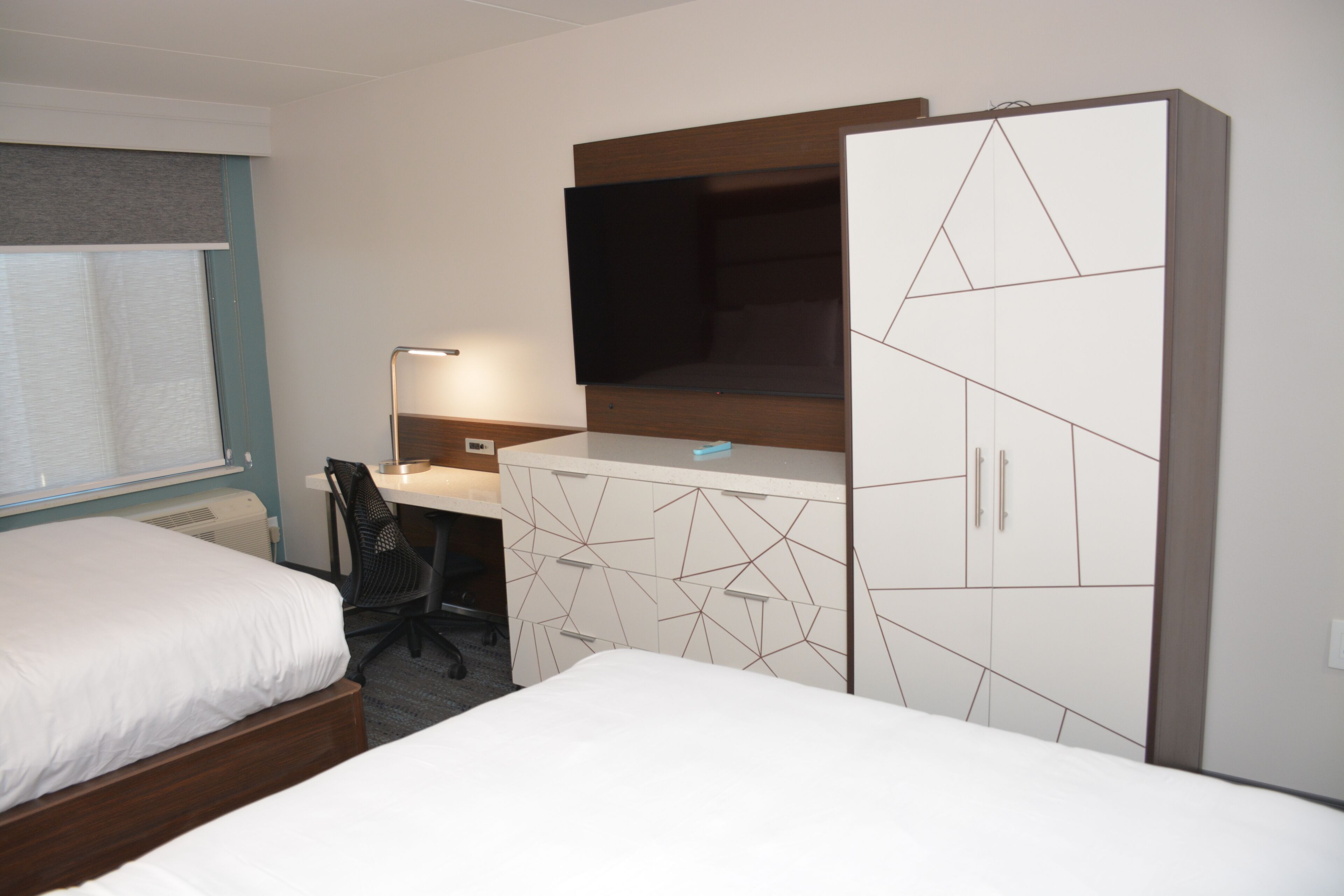 Ein Hotelzimmer mit zwei Betten, einem Schreibtisch, einem Sessel, einem Fernseher und einem Kleiderschrank.