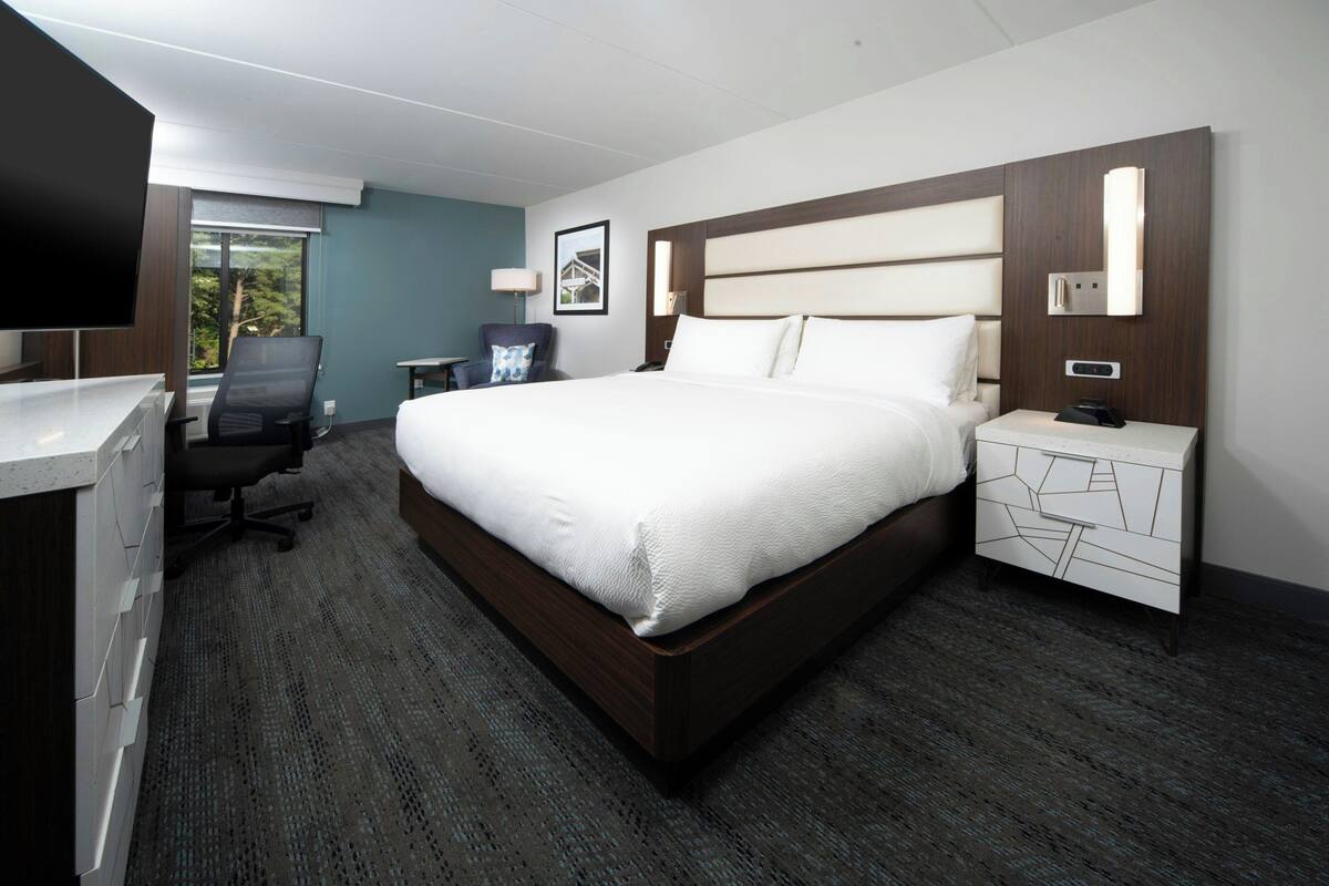 A hotel room with a large bed, a desk with a chair, a TV, and a nightstand with a phone.