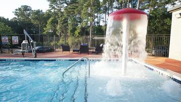A swimming pool with a water fountain, surrounded by a fence and chairs.