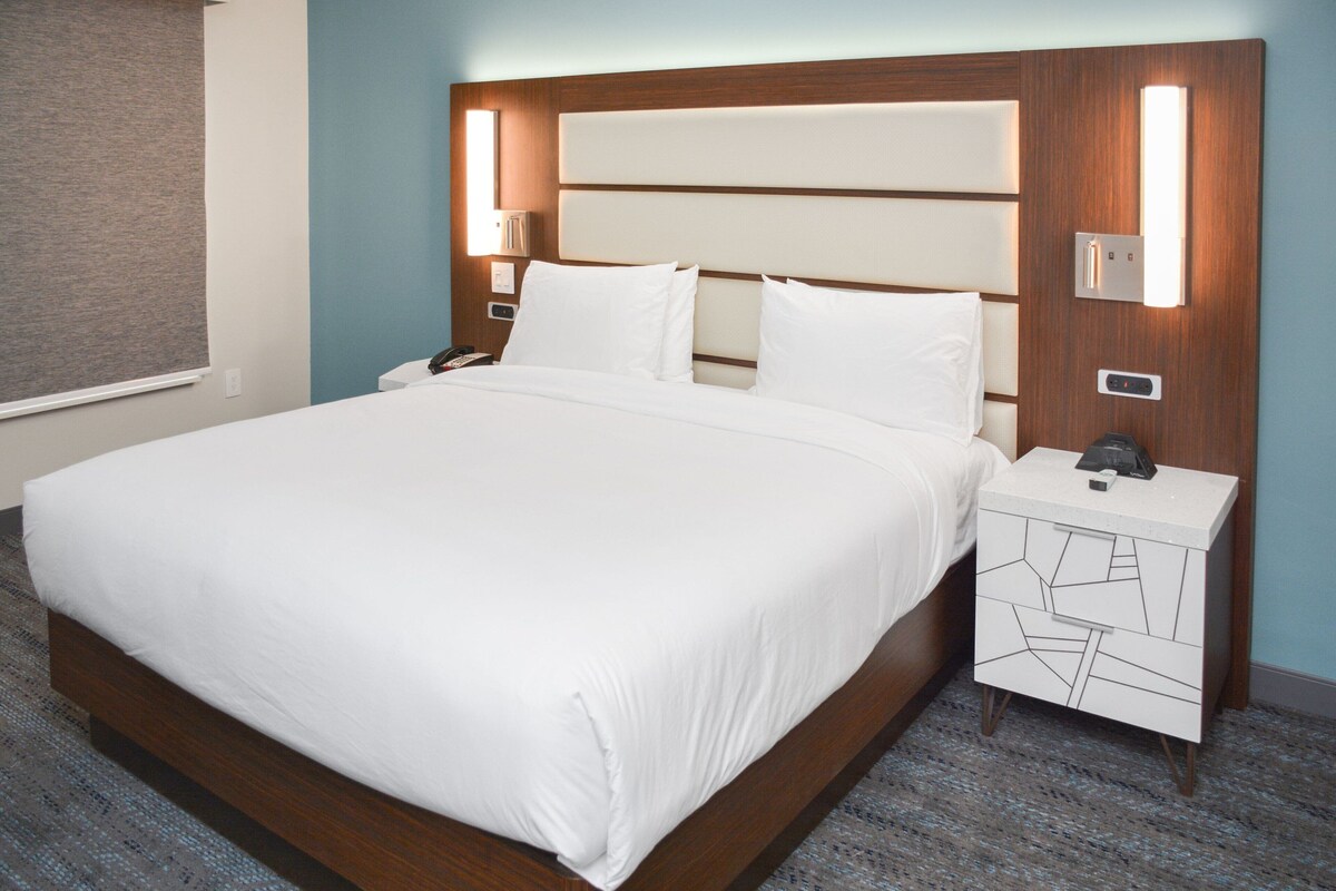 A neatly made bed with a wooden headboard, two bedside tables with lamps, and a patterned drawer unit.