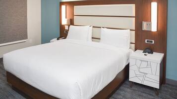 Una cama bien tendida con un cabecero de madera, dos mesitas de noche con lámparas y un mueble con cajones estampado.