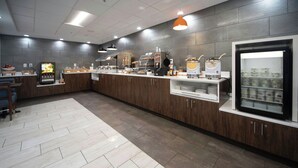A modern breakfast area with a long counter, a refrigerator, and various food items. - Four Points by Sheraton Fayetteville Fort Bragg (Fayetteville)