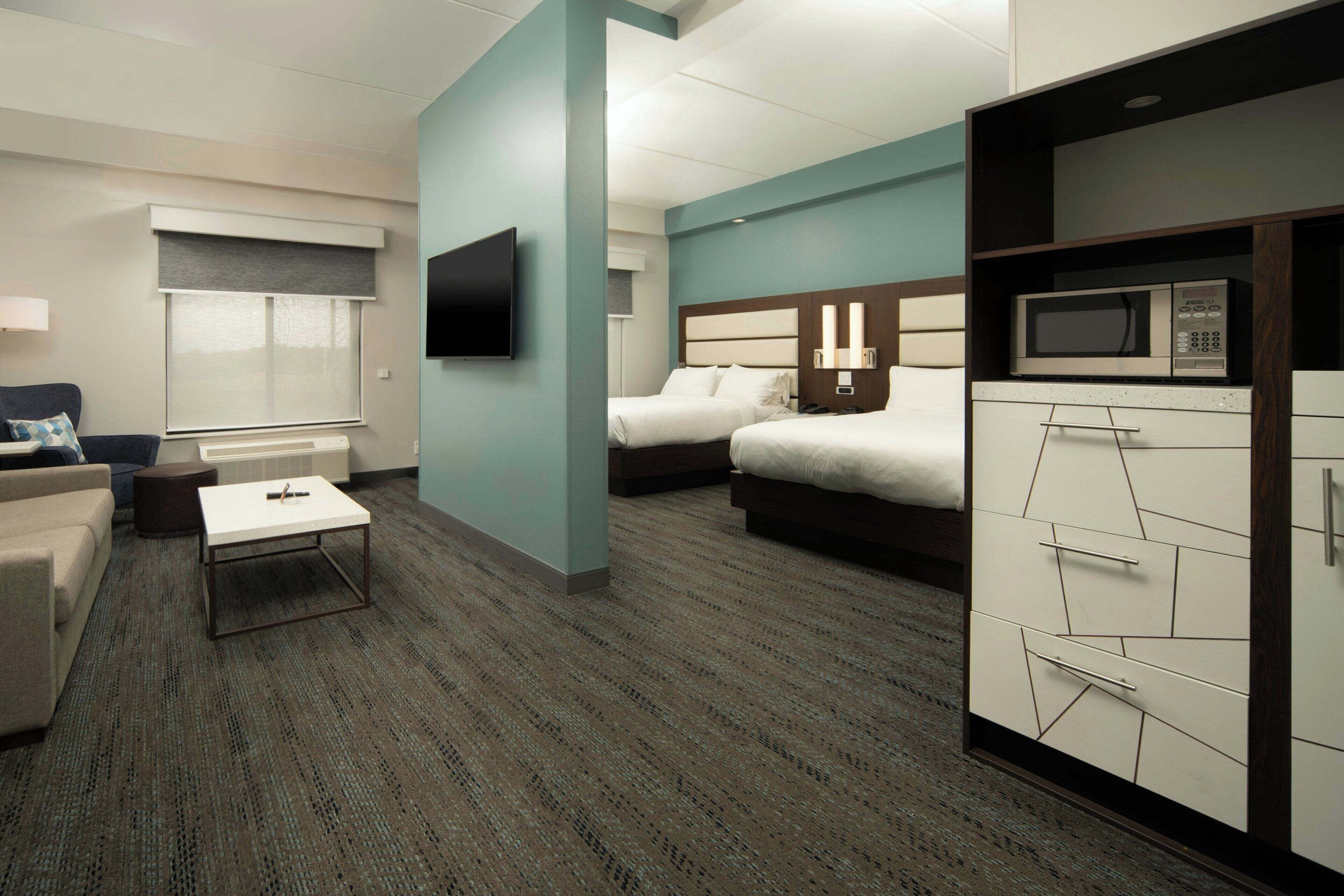 A hotel room with a flat-screen TV, two beds, a sofa, a coffee table, and a microwave.