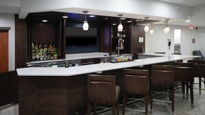 A modern bar area with a long counter, multiple bar stools, and a variety of bottles on shelves. - Four Points by Sheraton Fayetteville Fort Bragg (Fayetteville)