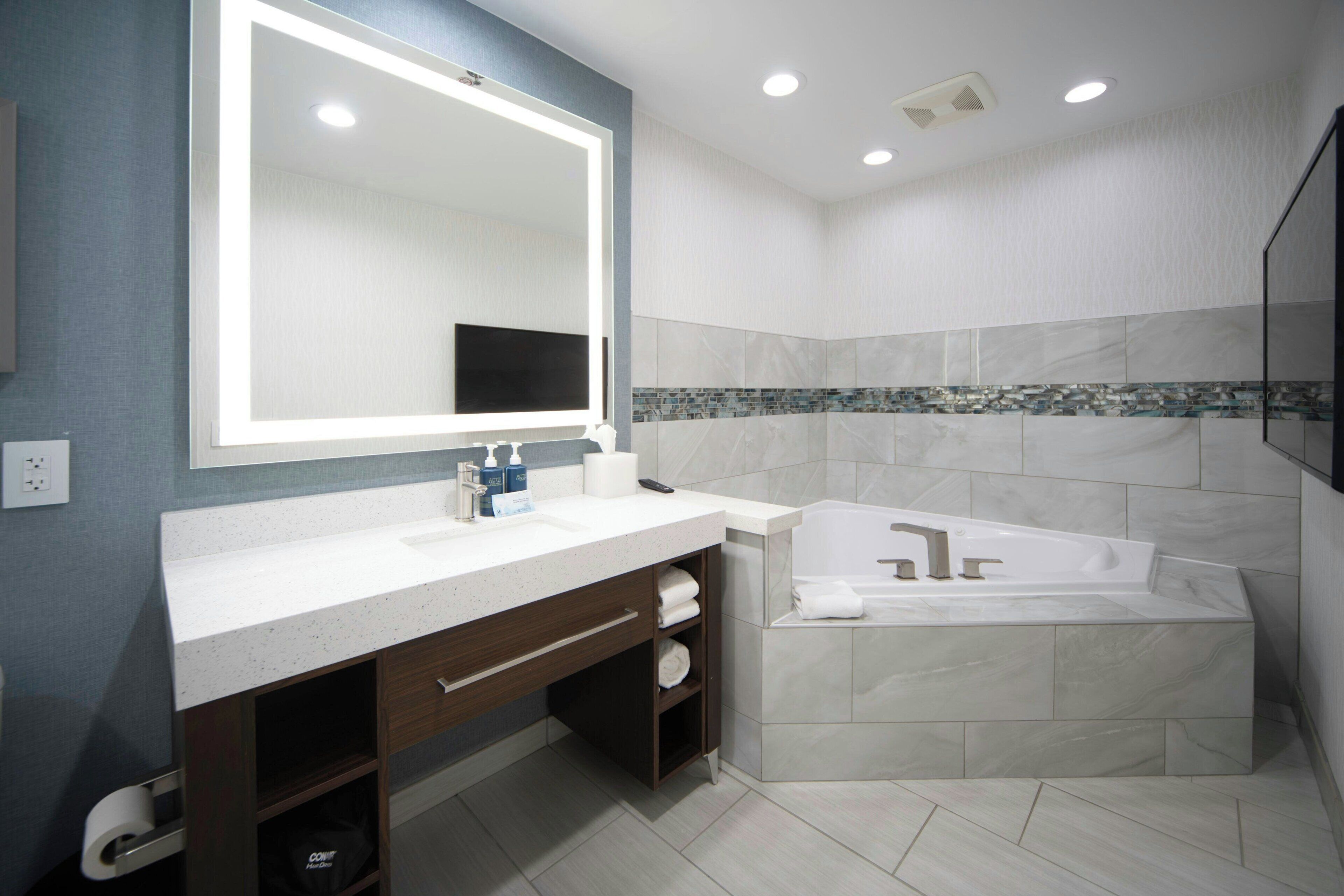 A modern bathroom with a large mirror, a bathtub, and a vanity with a sink.