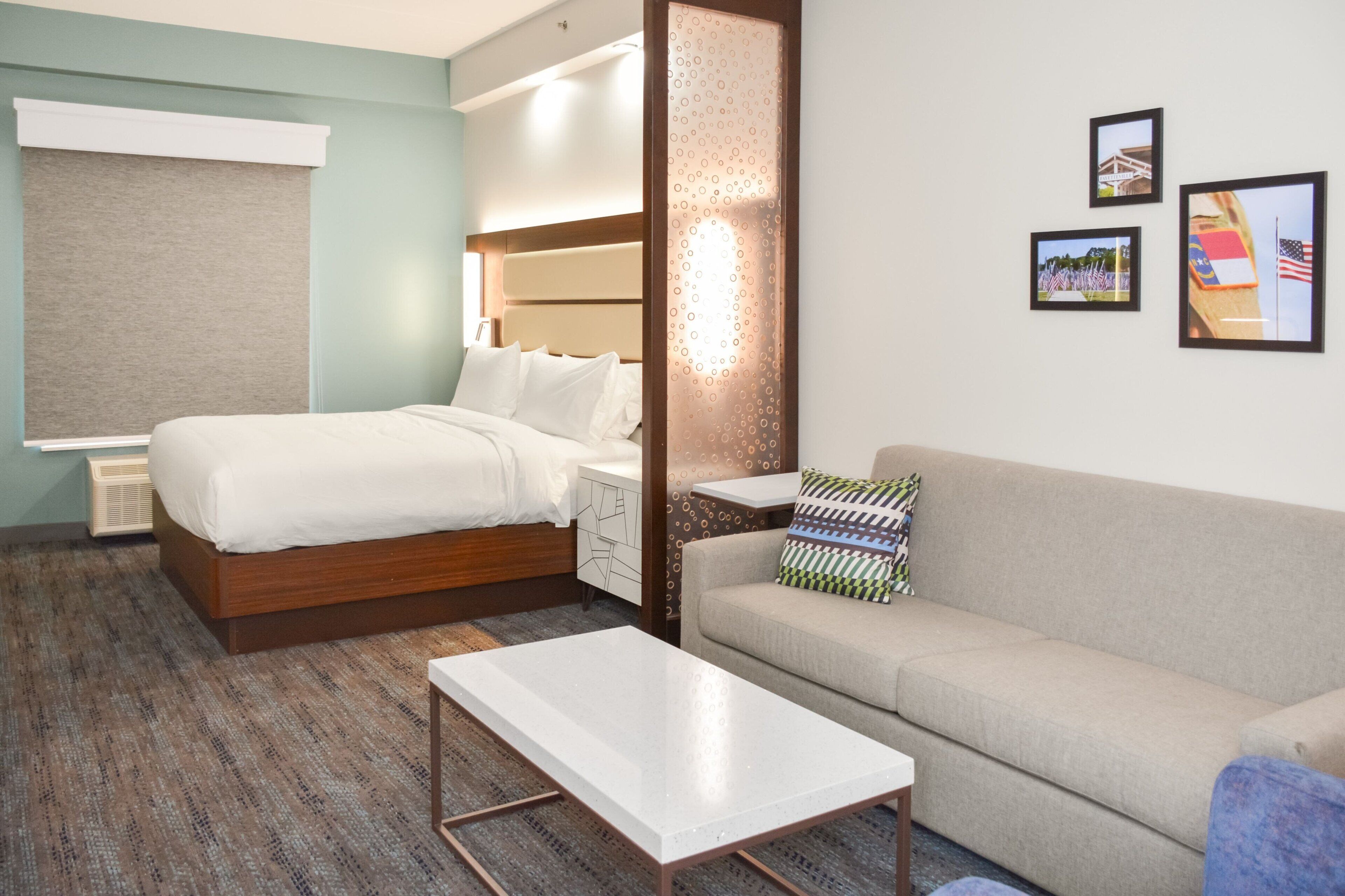 A hotel room with a bed, a sofa, a coffee table, and a wall with three framed pictures.