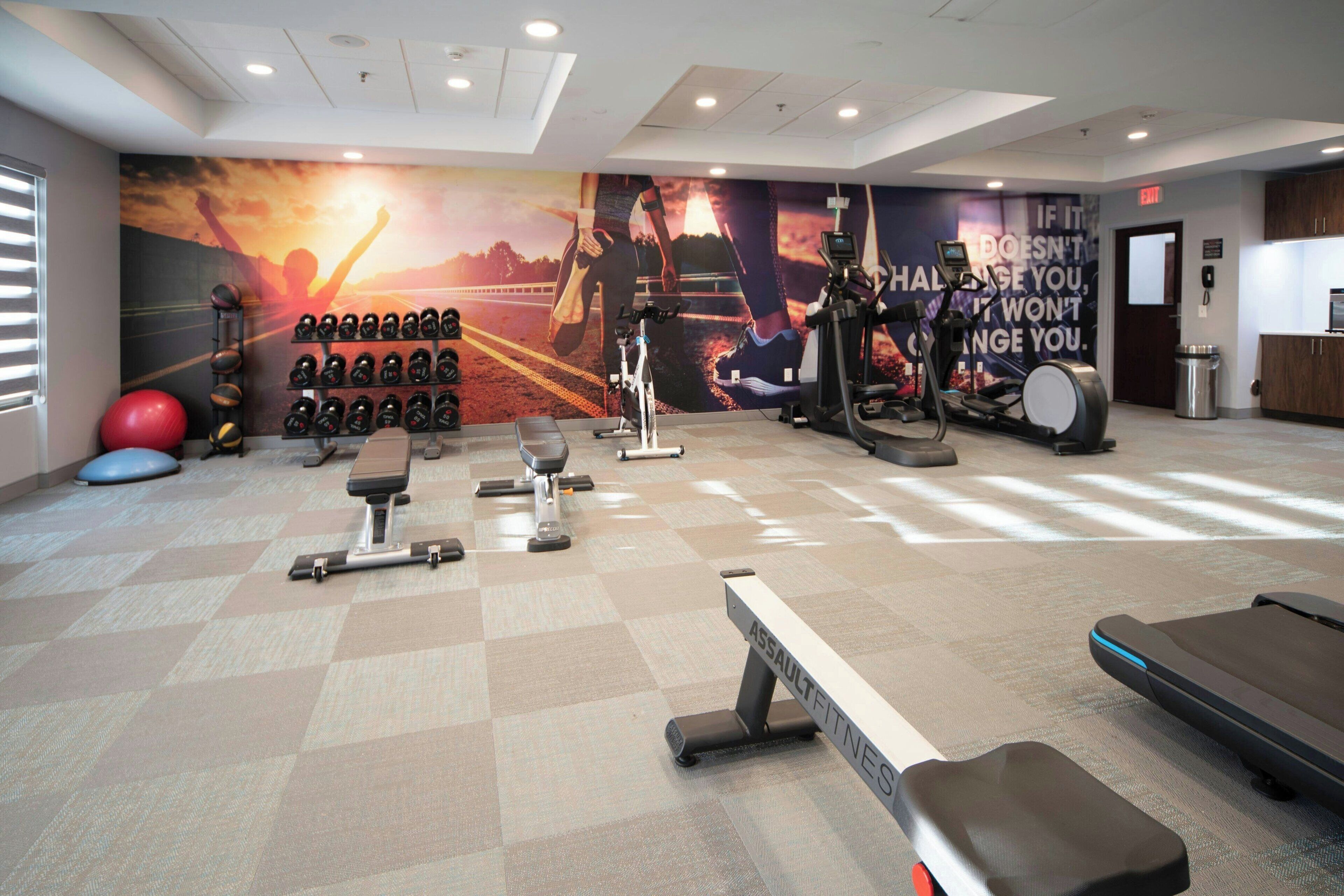 A gym with exercise equipment, a wall mural, and a bench.