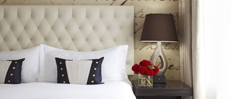 Una cama bien hecha con un cabecero capitonado, ropa de cama blanca y almohadas azules con botones dorados.
