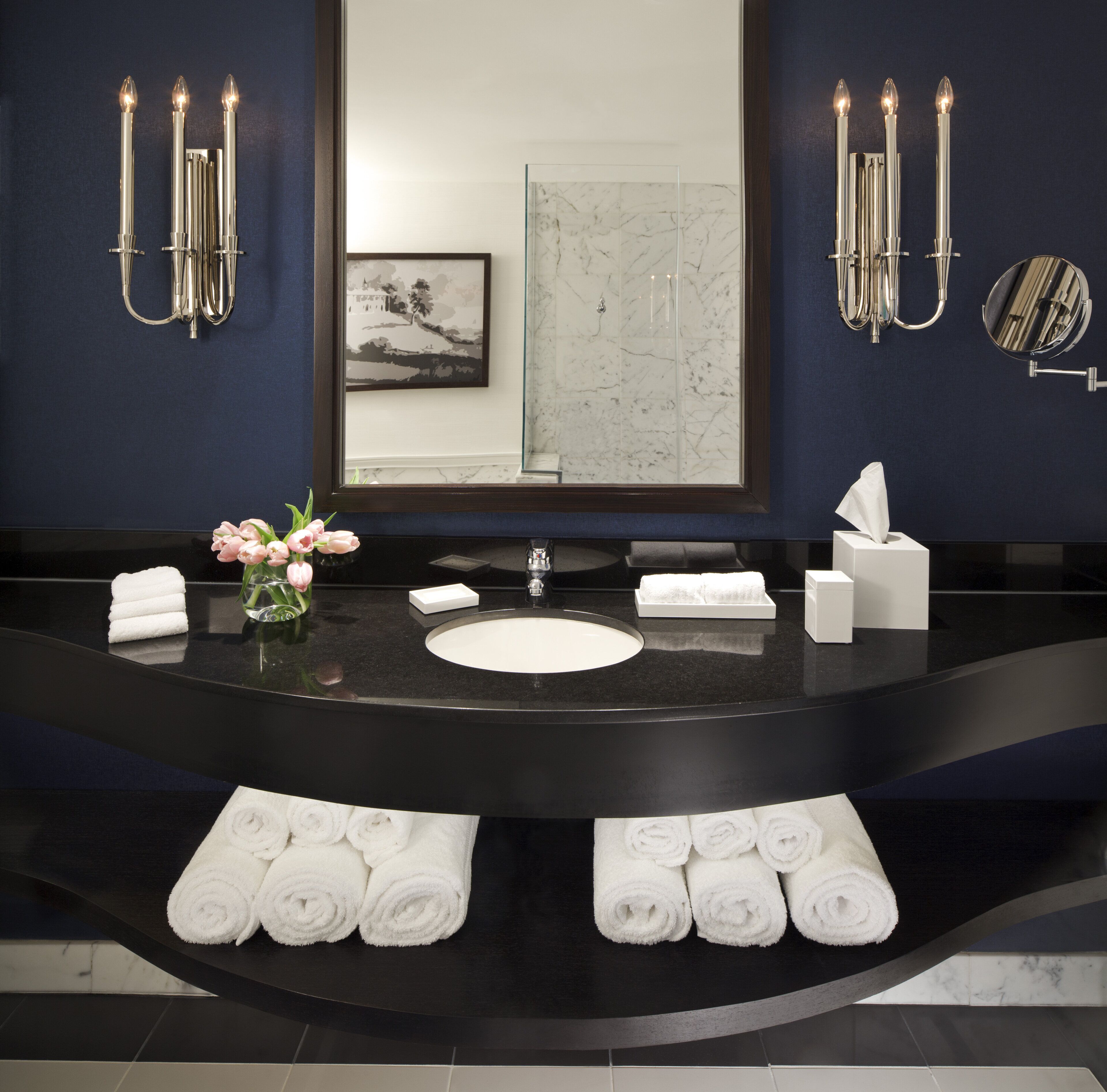 A modern bathroom with a black countertop, white sink, and multiple white towels.