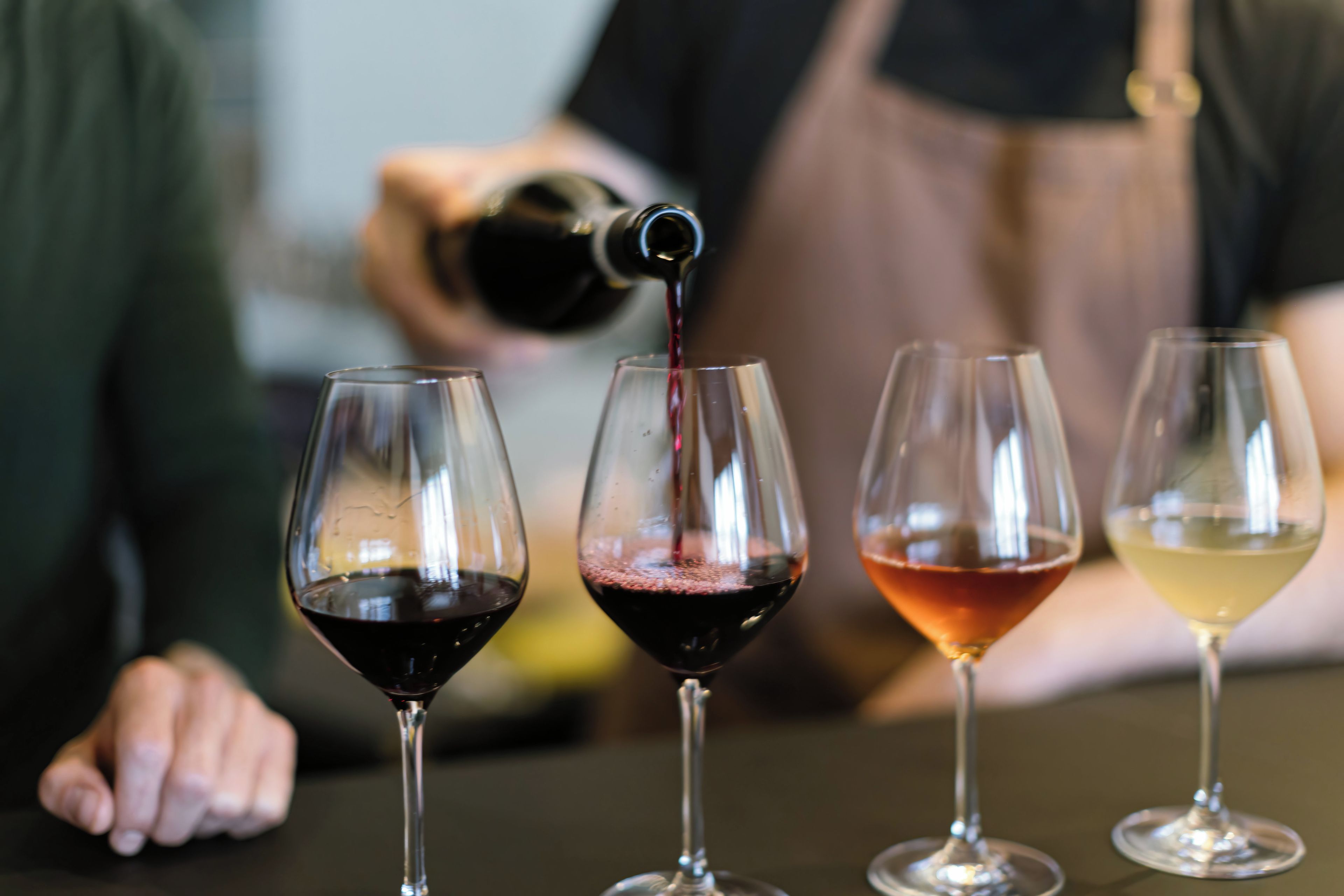 Four wine glasses on a table, each with a different color of liquid.