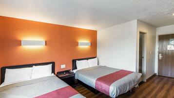 A hotel room with two beds, a wooden floor, and a door to the right.