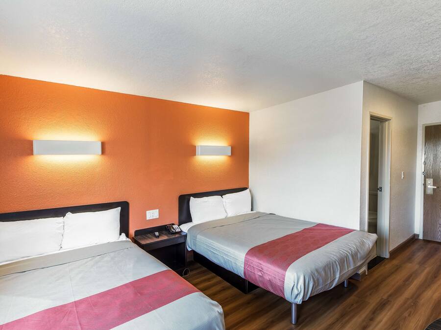 A hotel room with two beds, a wooden floor, and a door to the right.