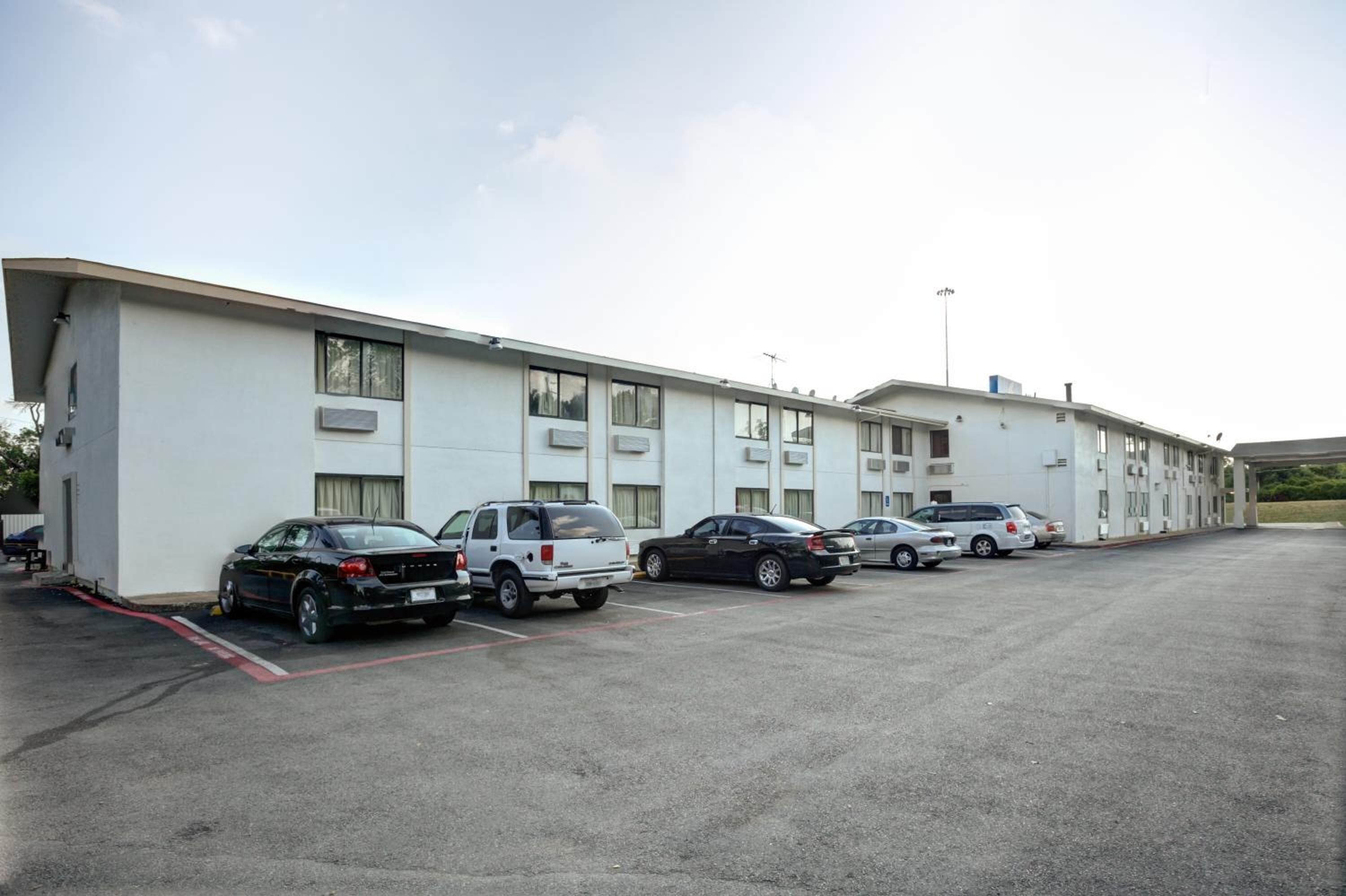 Un motel con una fila de espacios de estacionamiento y una hilera de habitaciones con ventanas amplias.