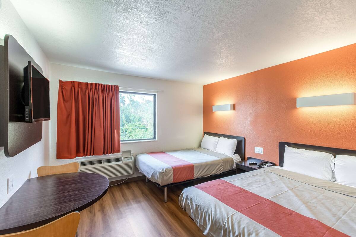 A hotel room with two beds, a TV, a desk, and a window with curtains.