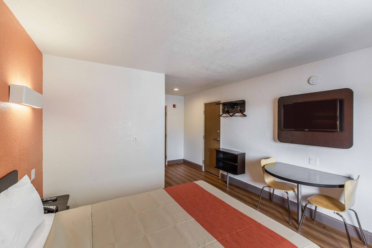 A hotel room with a bed, a desk with two chairs, a television, and a coat rack.