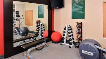 Uma academia com equipamentos de exercício, uma televisão e um espelho.
