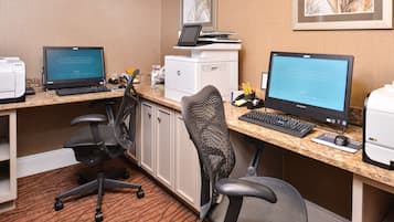 A hotel office with two desktop computers, a printer, and office chairs.
