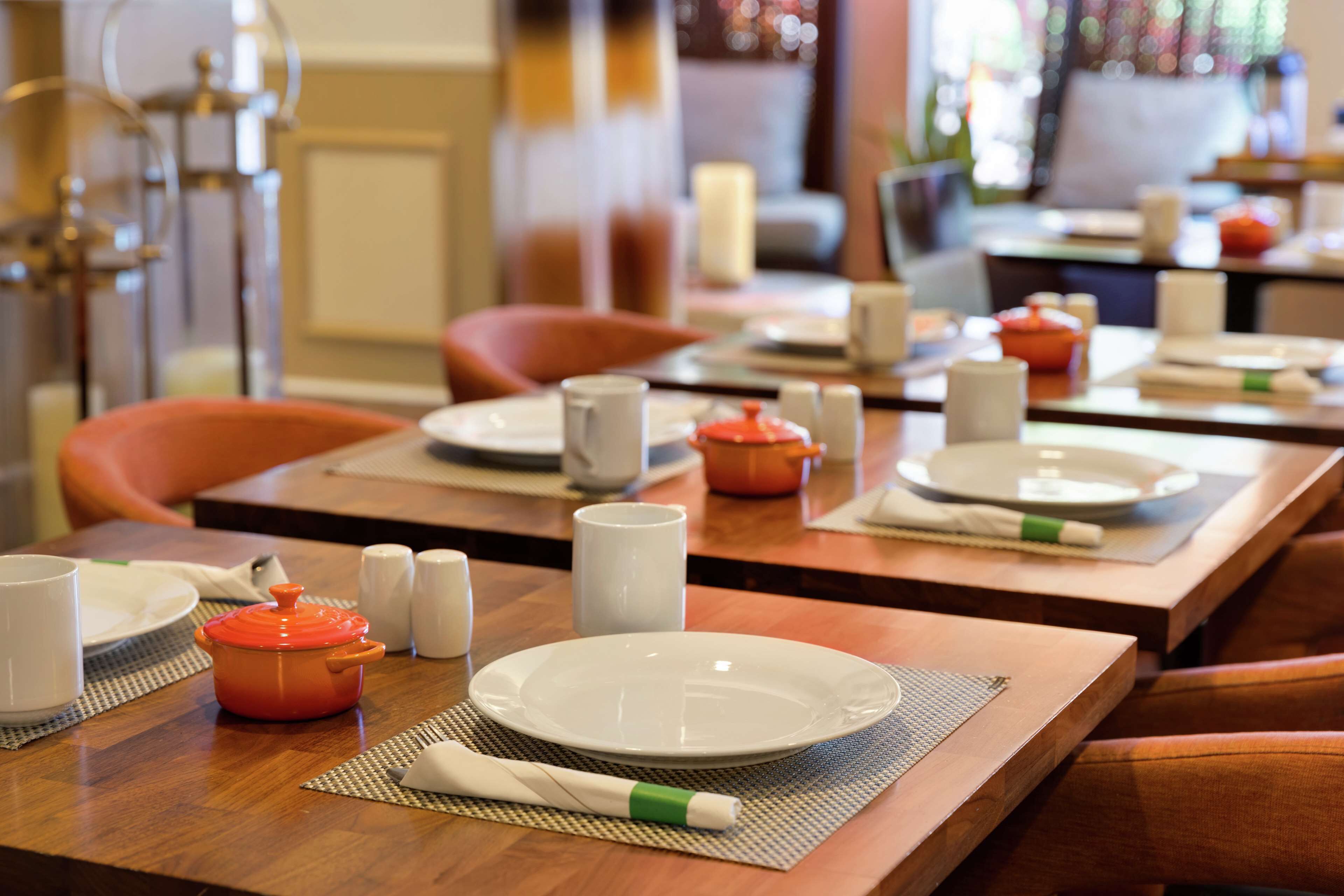 Une table à manger dressée avec des assiettes, un pot rouge, des salières et des poivrières, et une serviette blanche.