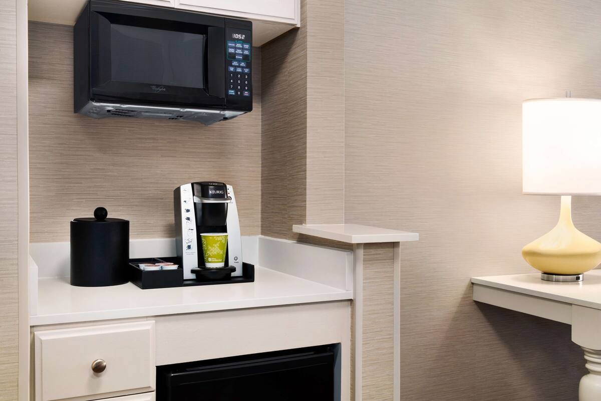A kitchenette with a microwave, coffee maker, and a lamp on the counter.