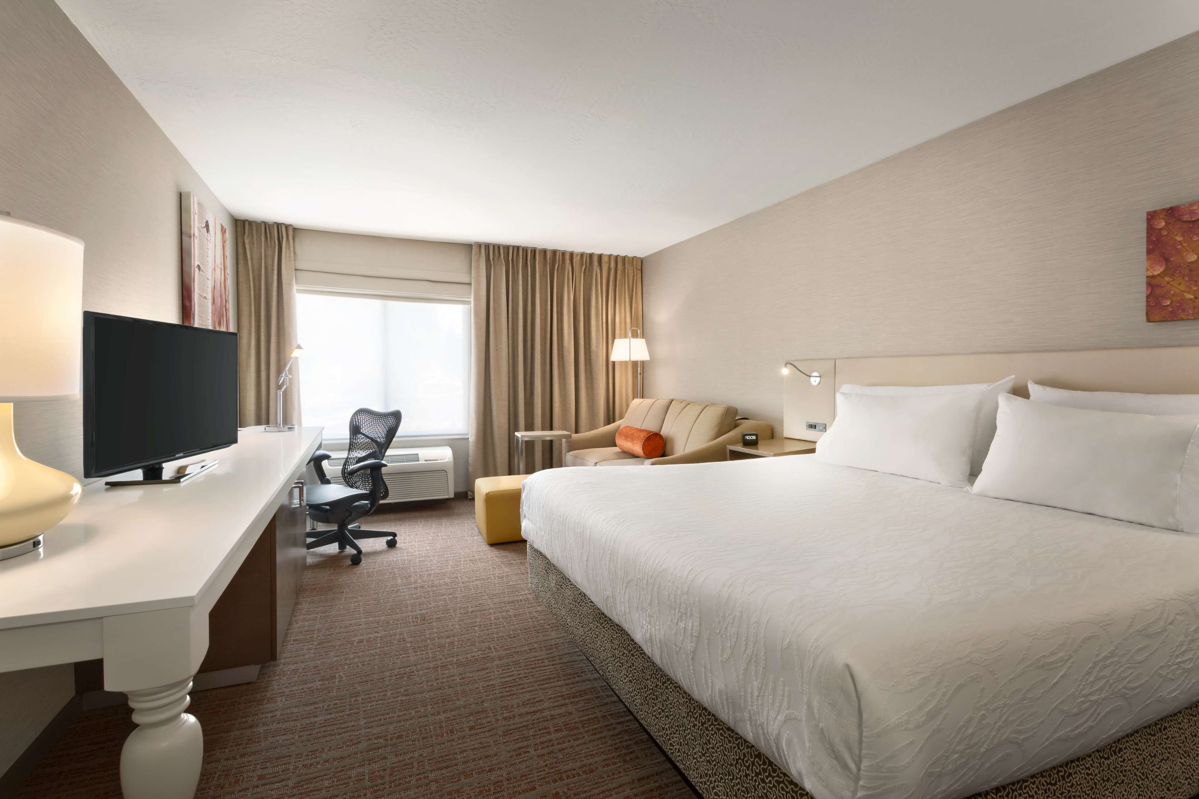 A hotel room with a large bed, a desk with a television, a chair, and a window with curtains.