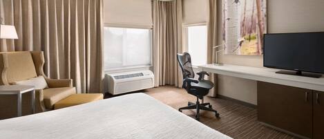 A hotel room with a bed, a desk, a chair, a television, and a window with curtains.