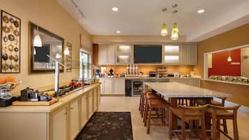 A modern kitchen with a central island, wooden chairs, and a large window.
