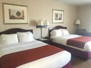 A hotel room with two beds, each with white linens and red bedspreads. There are two wall-mounted lamps on either side of the beds, and two framed pictures above the beds.