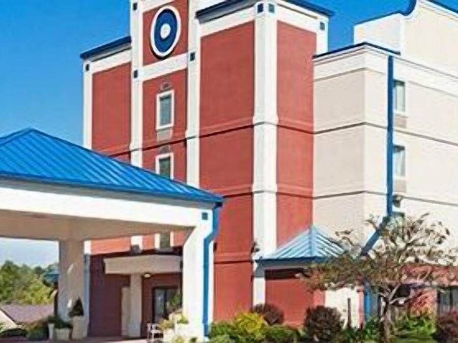 A hotel with a red and white facade, a covered entrance, and a clock tower.