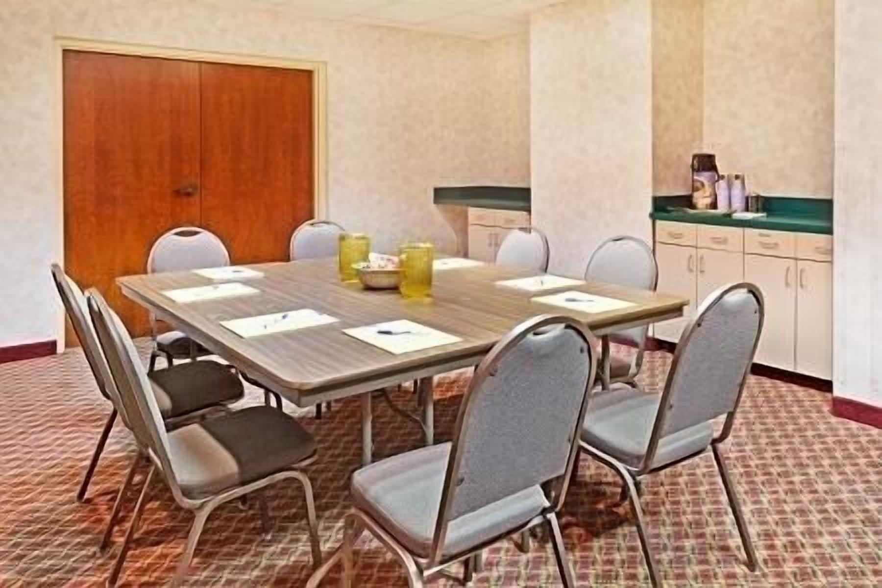 A conference room with a wooden table, six chairs, and a closed door.