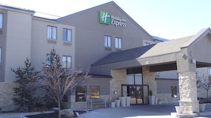 A Holiday Inn Express building with a covered entrance, stone pillars, and a bench outside. - Holiday Inn Express Kansas City-Bonner Springs by IHG (Bonner Springs)