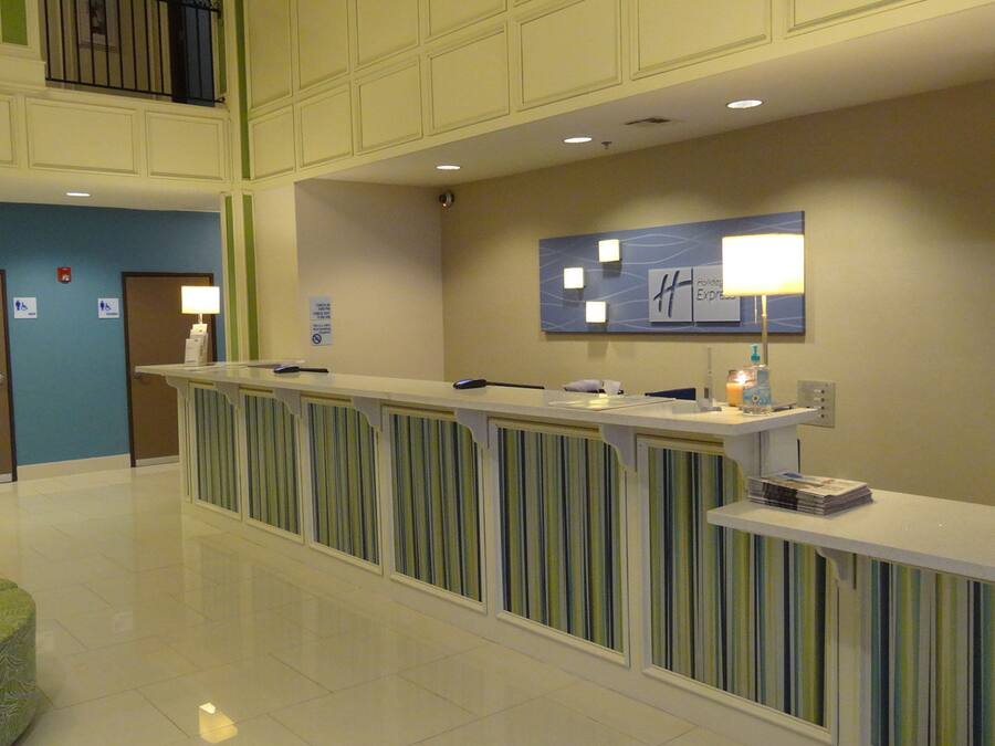 A hotel reception area with a reception desk, a check-in counter, a seating area with a green chair, and a wall-mounted sign indicating the Holiday Inn Express.