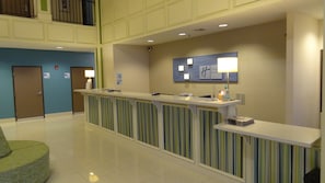 A hotel reception area with a reception desk, a check-in counter, a seating area with a green chair, and a wall-mounted sign indicating the Holiday Inn Express. - Holiday Inn Express Kansas City-Bonner Springs by IHG (Bonner Springs)