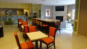 A hotel dining area with multiple tables and chairs, a bar area, and a fireplace. - Holiday Inn Express Kansas City-Bonner Springs by IHG (Bonner Springs)