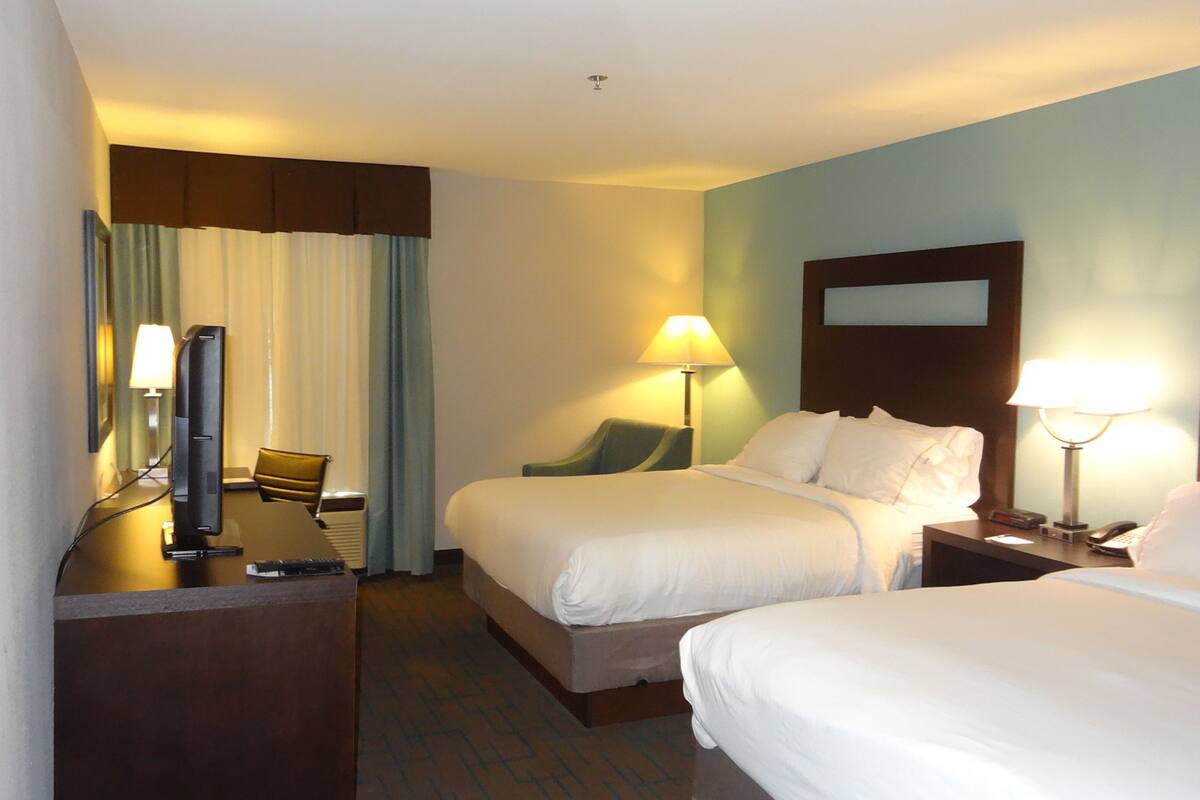 A hotel room with two beds, a desk with a computer, a chair, and two lamps.
