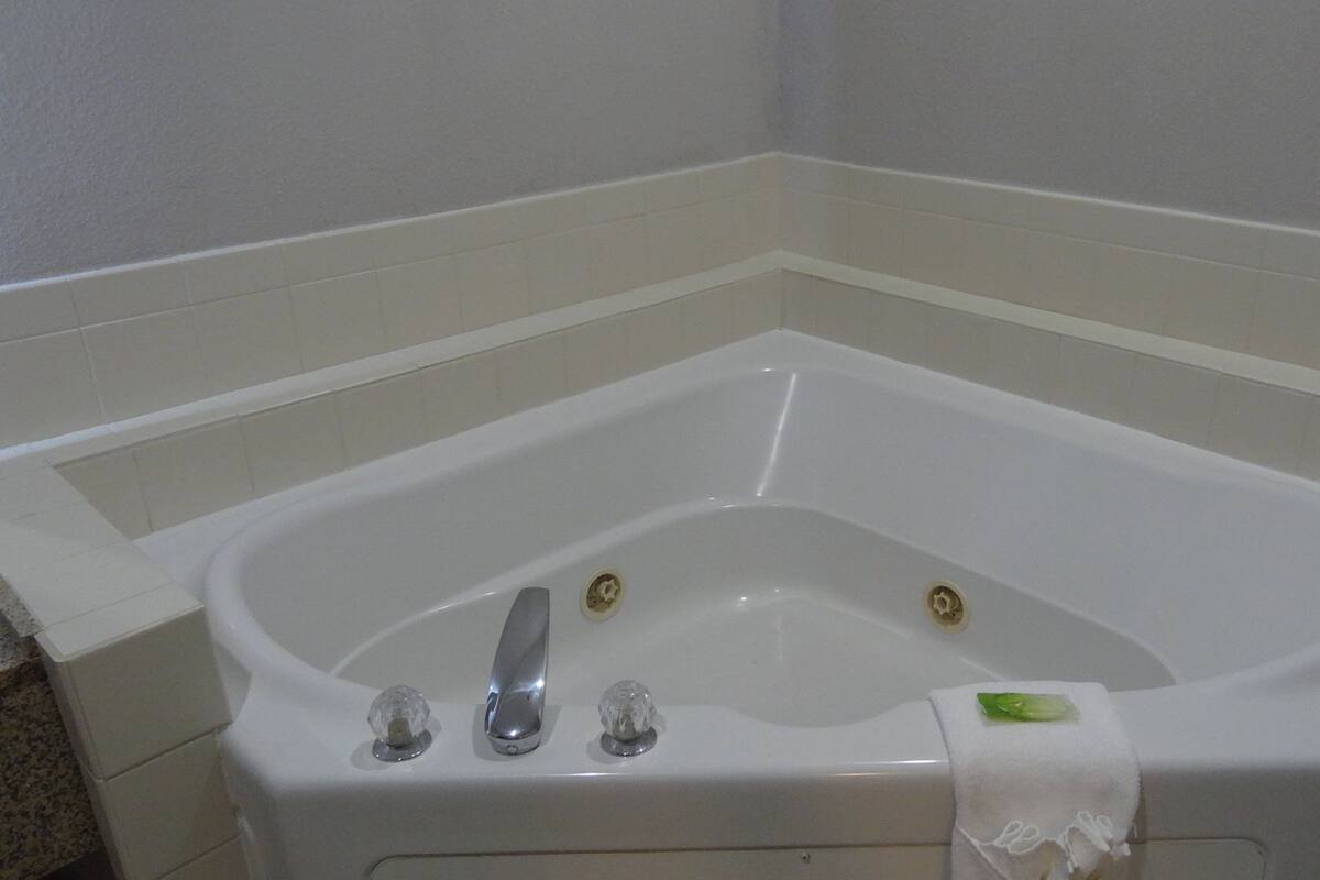 A corner bathtub with a faucet and two knobs, a towel on the side, and a green object on the edge.