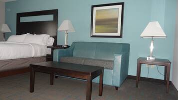 A hotel room with a bed, a blue sofa, a wooden table, and two bedside lamps.