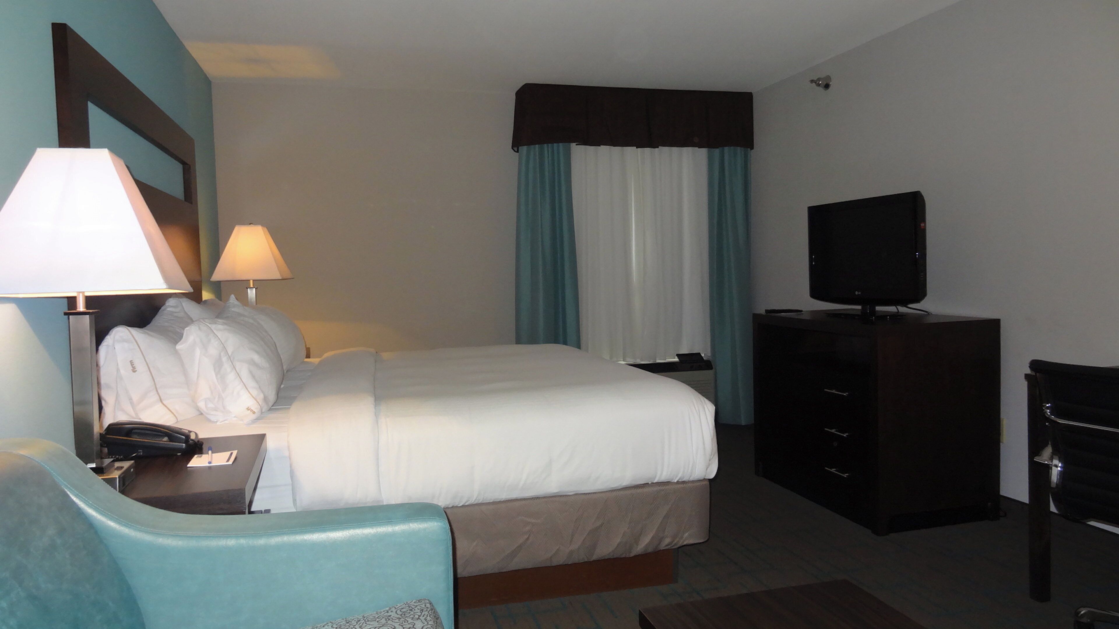 Una camera d'albergo con un letto, una scrivania con una lampada, una televisione e una sedia.