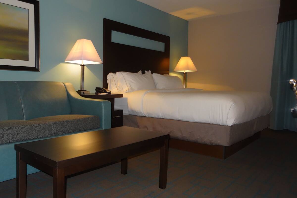 A hotel room with a bed, a sofa, a nightstand with a lamp, and a painting on the wall.