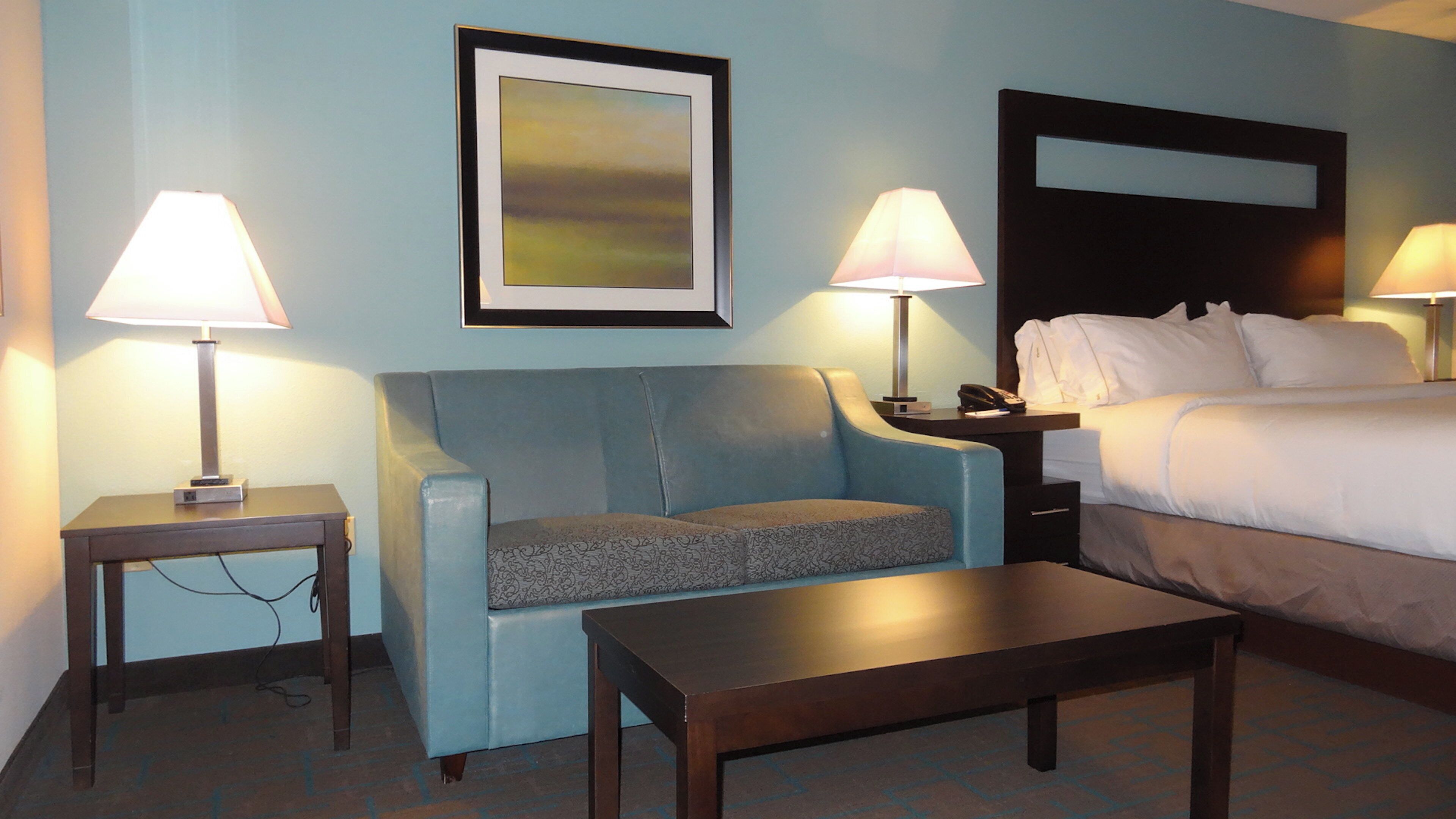 Una habitación de hotel con una cama, dos mesitas de noche con lámparas, un sofá y una pequeña mesa.