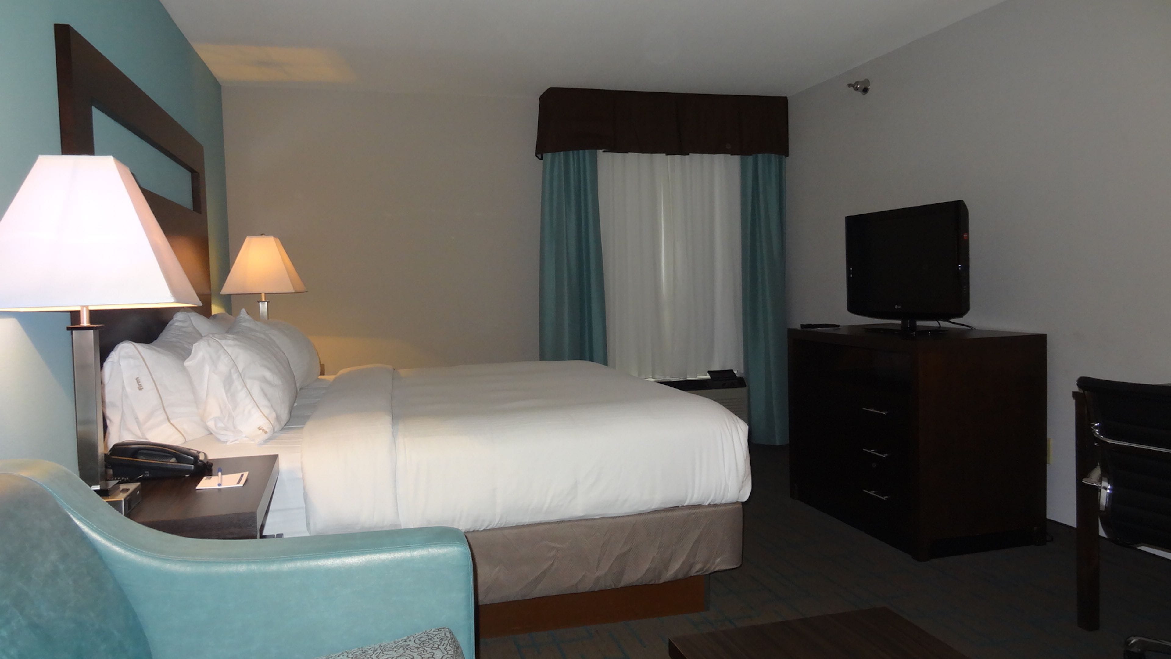 Ein Hotelzimmer mit einem Bett, einem Schreibtisch mit Lampe, einem Fernseher und einem Sessel.