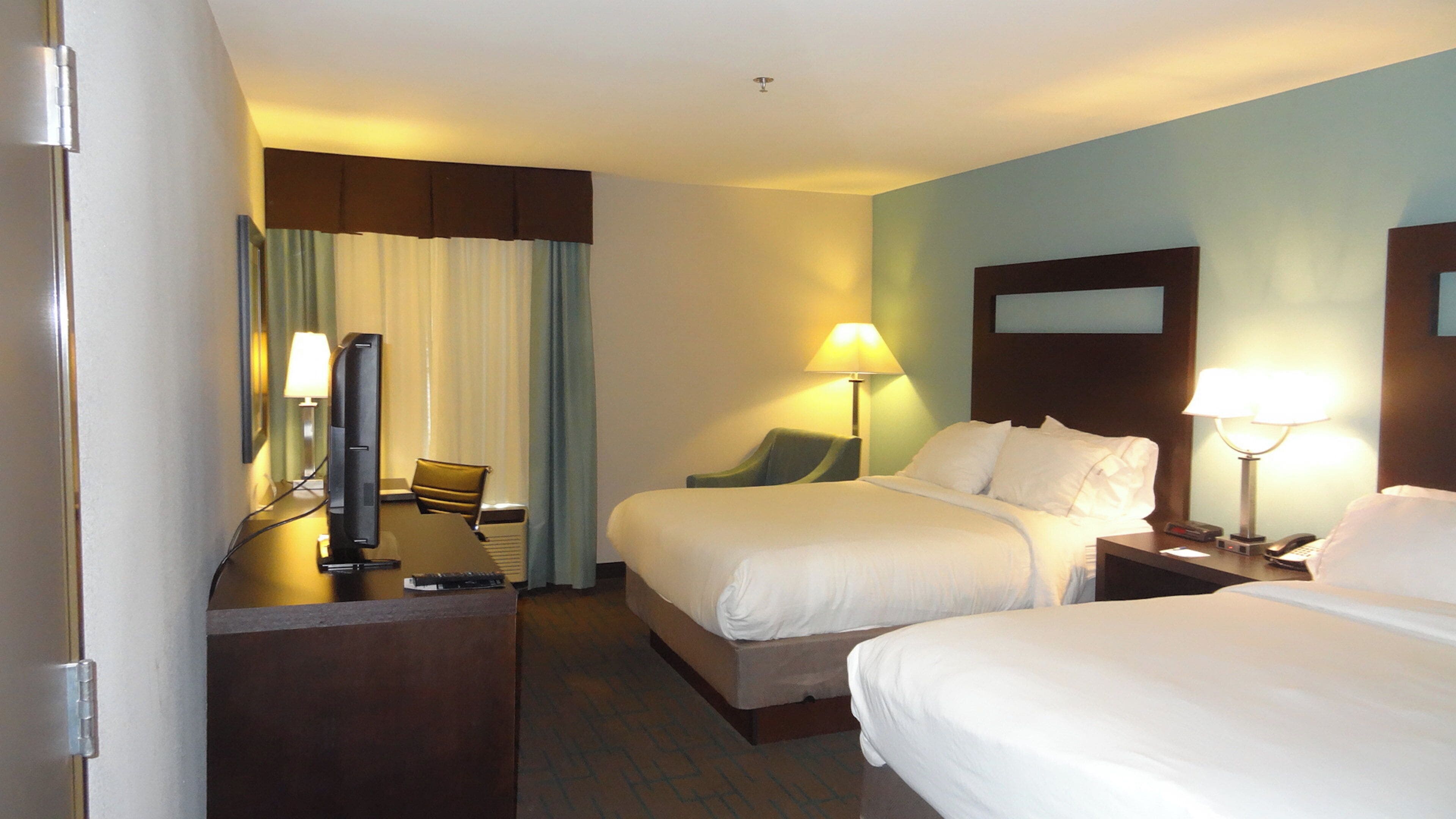 A hotel room with two beds, a desk with a computer, a chair, and a lamp.