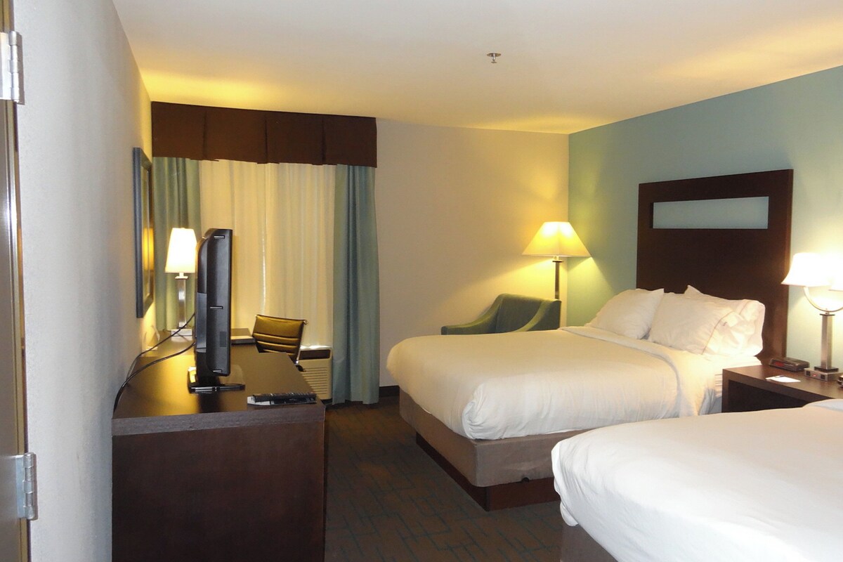 Habitación de hotel con dos camas, un escritorio con computadora, una silla y una lámpara.