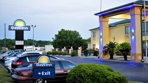 Un Days Inn con aparcamiento, un cartel de salida y una entrada con pilares iluminados.