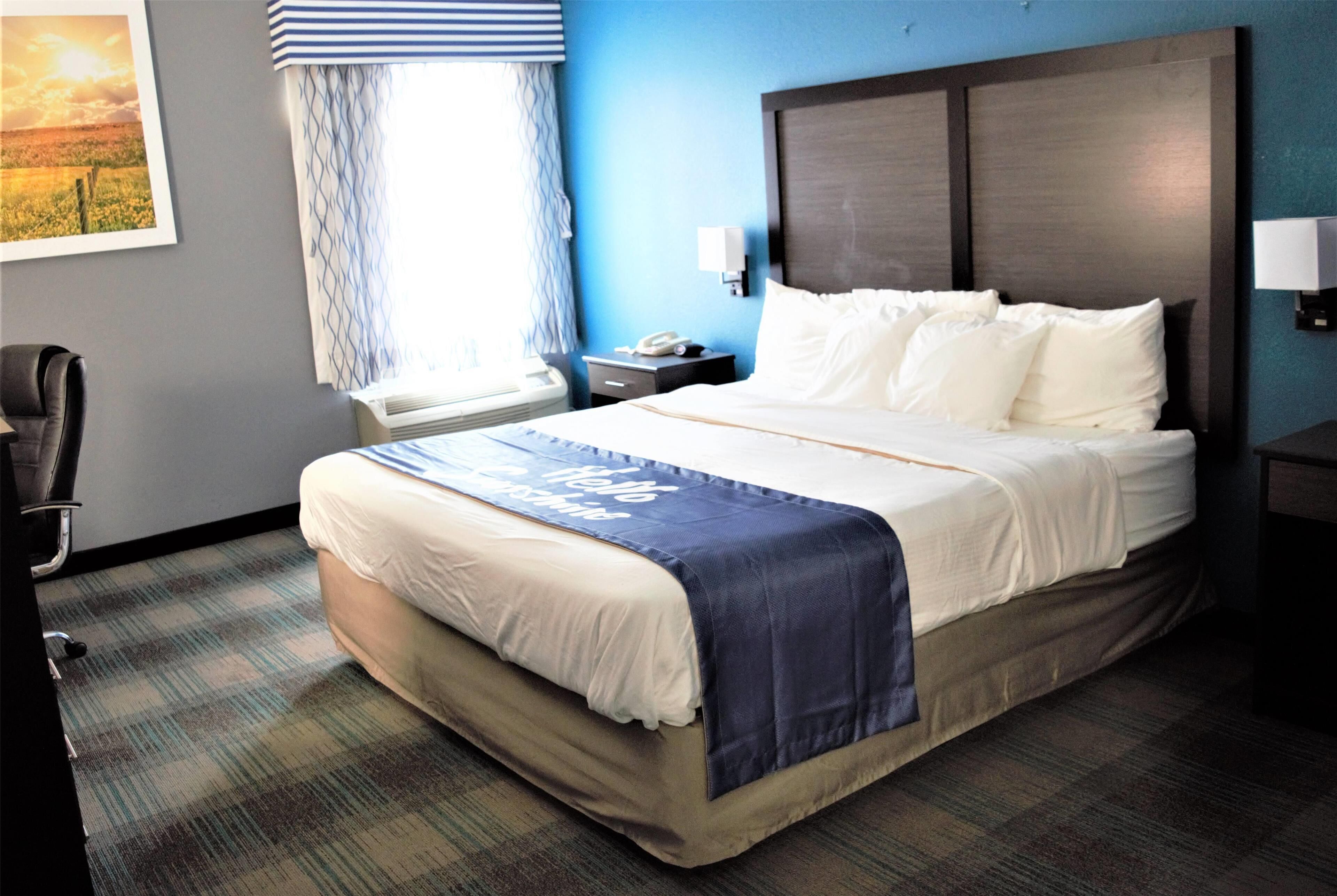 Une chambre d’hôtel avec un grand lit, un bureau, une chaise, une fenêtre avec des rideaux et un téléphone fixé au mur.