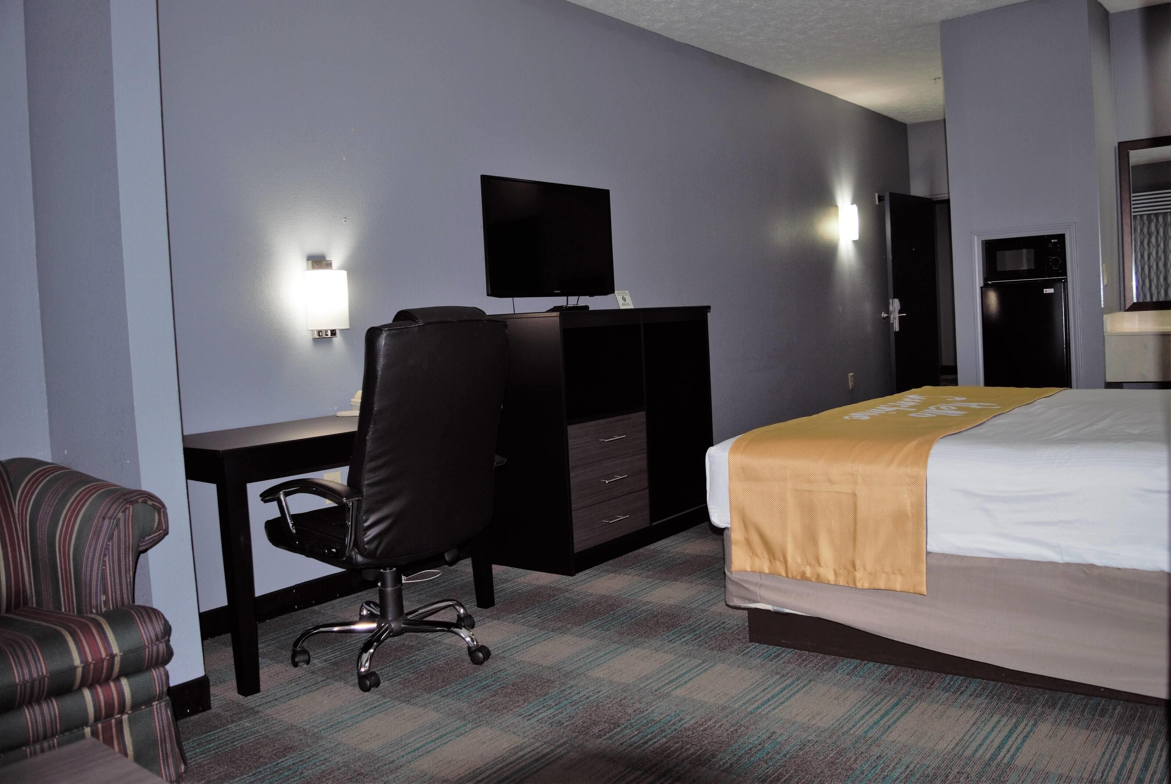 A hotel room with a bed, a desk with a TV, a chair, and a wardrobe.