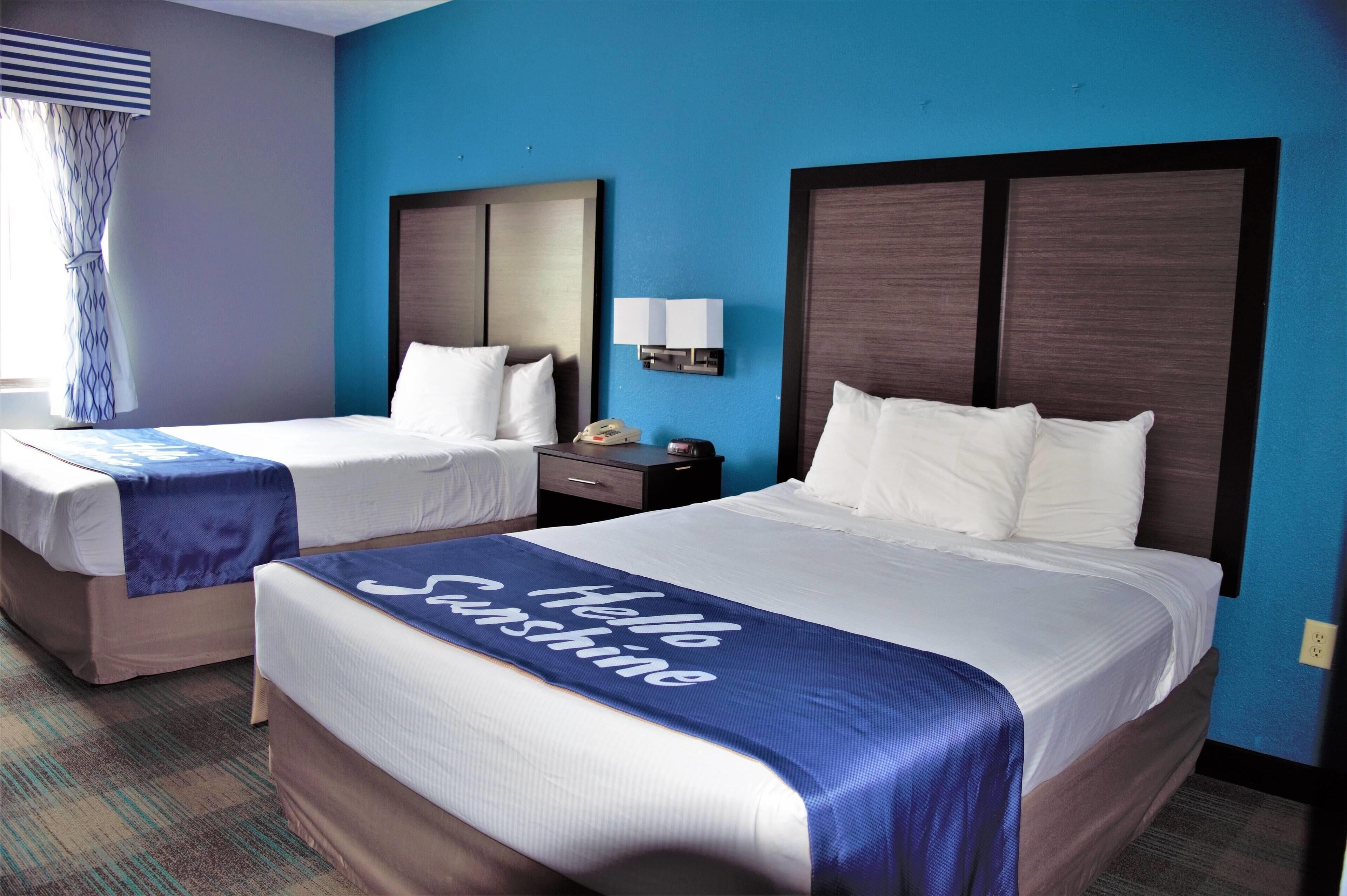 A hotel room with two beds, a nightstand, a lamp, and a window with curtains.