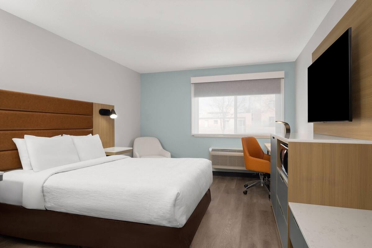 Habitación de hotel con cama, escritorio, silla, televisión y ventana.