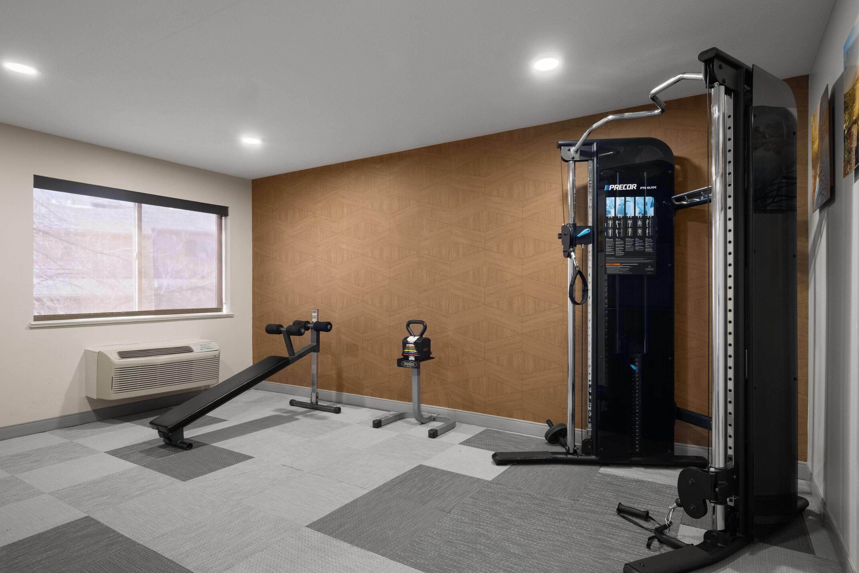Un gimnasio con aire acondicionado de pared, una banca, una estructura para sentadillas y una barra para dominadas.