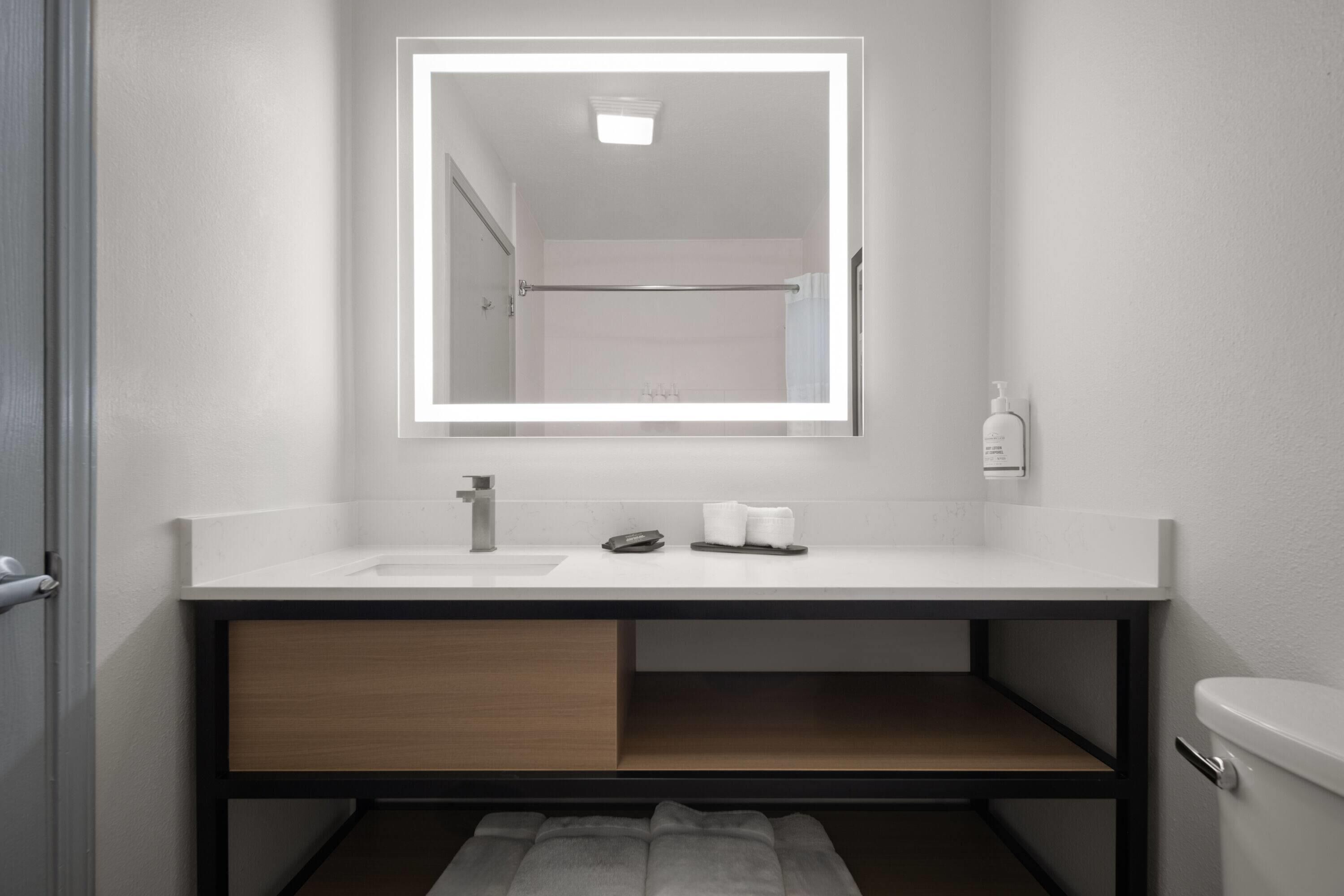 A modern bathroom with a white vanity, a mirror, a towel rack, and a toilet.
